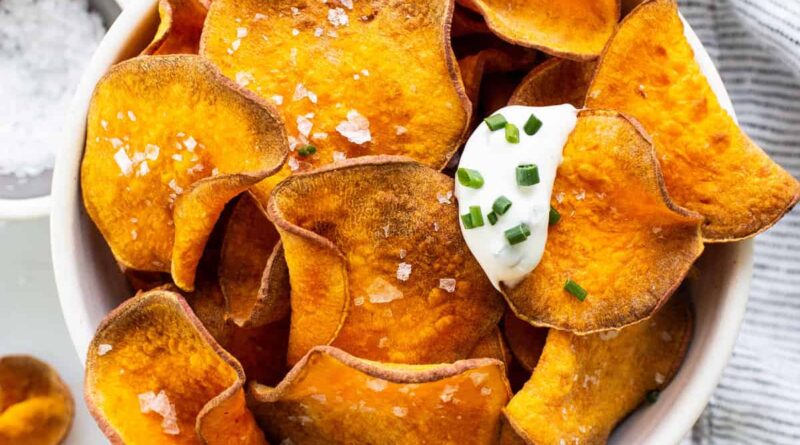 Sweet potato chips in a bowl with sour cream and parsley.