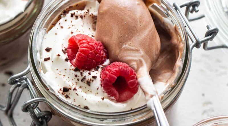 Chocolate mousse in jars with whipped cream and raspberries.