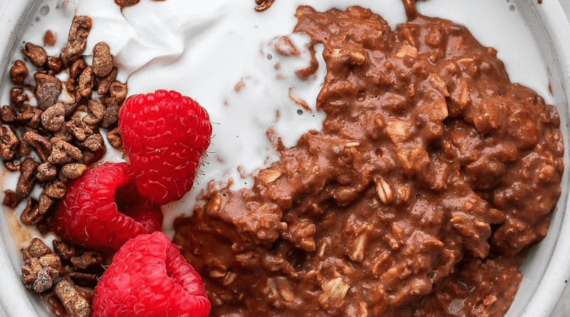 A bowl of chocolate protein oatmeal with raspberries and whipped cream.