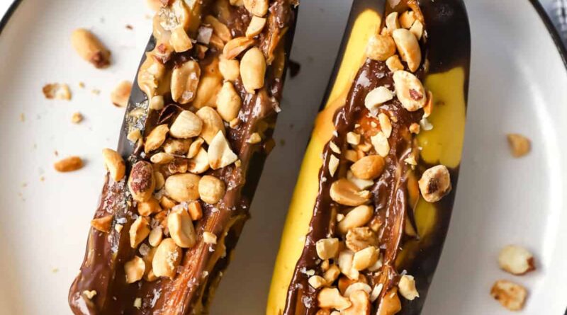 Two bananas with peanuts and chocolate on a plate.