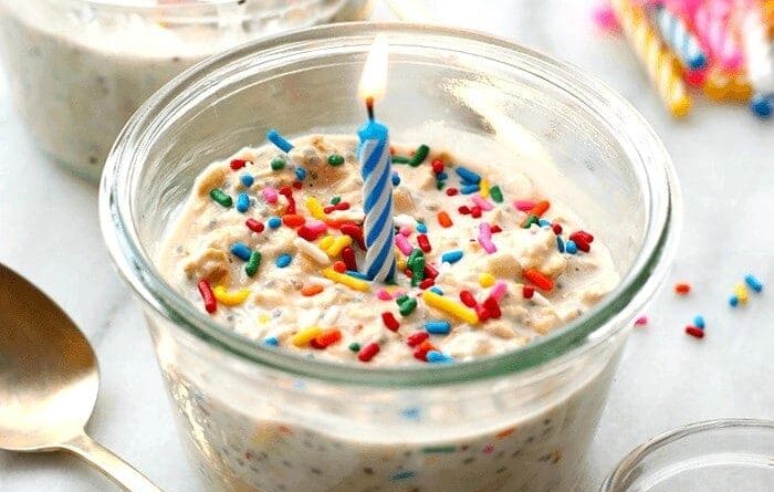 A birthday cake in a jar with sprinkles and a candle made from cake batter overnight oats.