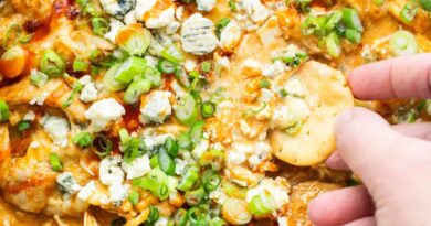 A person dipping chips into a bowl of buffalo chicken dip.