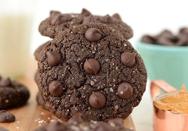 Flourless Double Chocolate Peanut Butter Cookies displayed on a cutting board accompanied by a glass of milk.