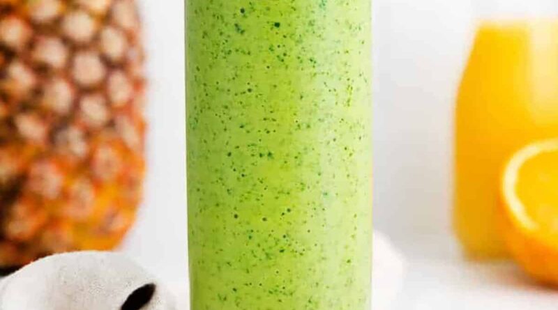 A green spinach smoothie in a glass with oranges and pineapples.