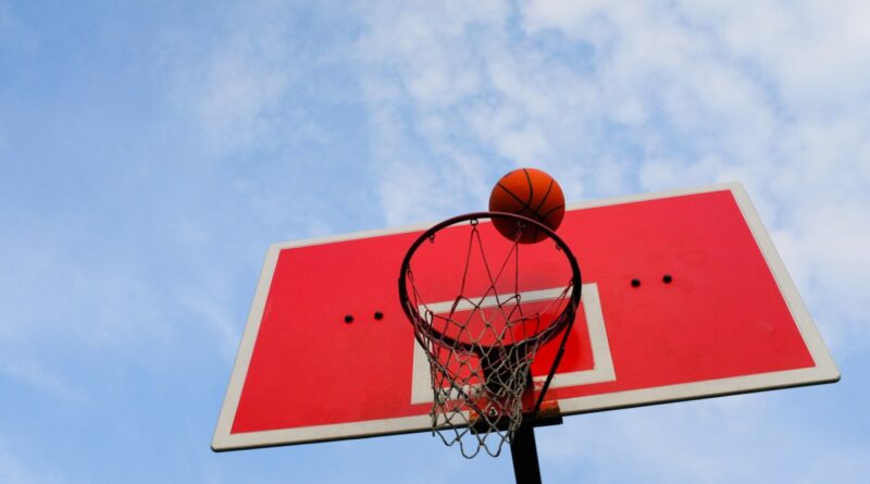a basketball flies into the basket, against the blue sky, in an open area.