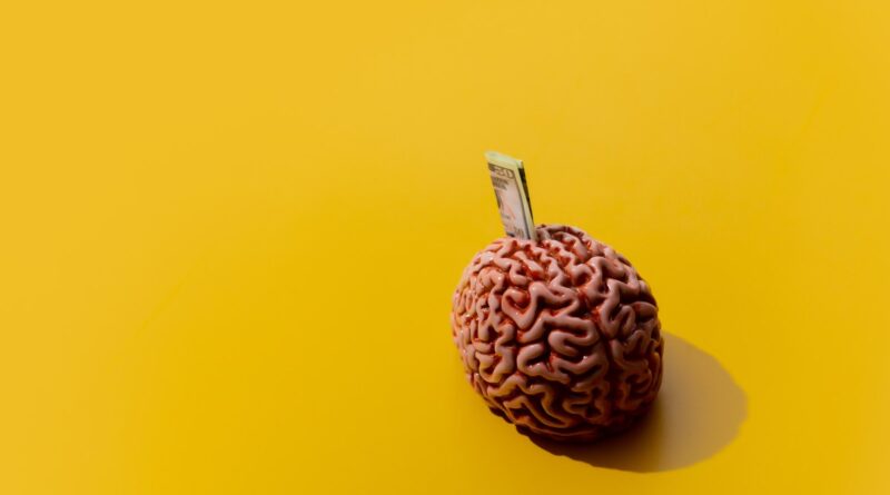 Image of money sticking out of a brain against a yellow background