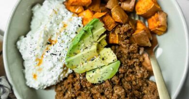 A bowl containing ground beef, roasted sweet potatoes, cottage cheese with hot sauce, and avocado slices, topped with black pepper.