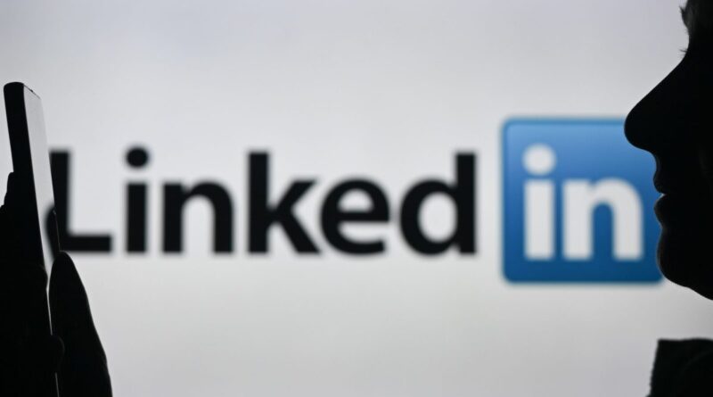 An image of a woman holding a cell phone in front of a LinkedIn logo displayed on a computer screen.