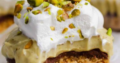 A dessert bar with a crumbly base, chocolate layer, creamy filling, whipped topping, and chopped pistachios, with a bite taken out of it.