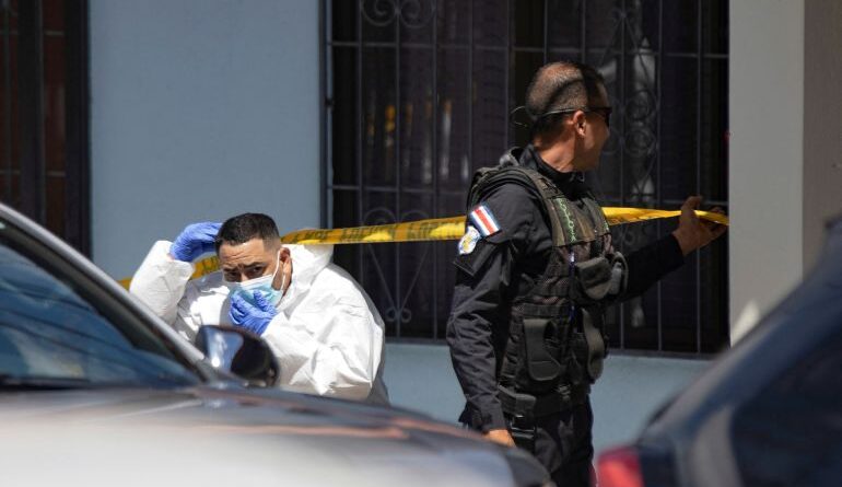 A forensic tech ducks under crime scene tape.