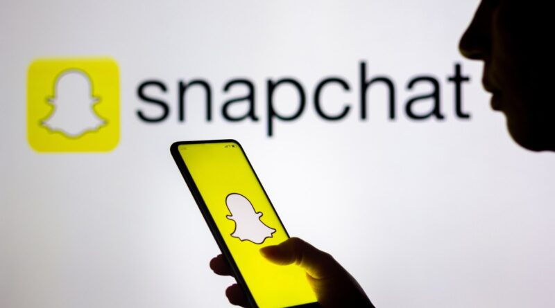 In this photo illustration, a woman's silhouette holds a smartphone with the Snapchat logo displayed on the screen and in the background.