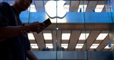 A pedestrian uses a smartphone while walking past an Apple store and logo in Hong Kong.