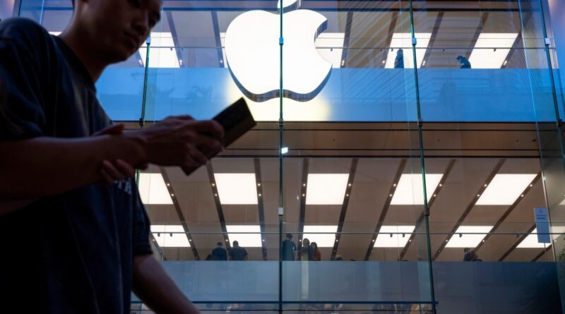 A pedestrian uses a smartphone while walking past an Apple store and logo in Hong Kong.