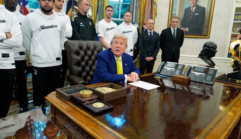Donald Trump sits at the Resolute Desk, with members of the Juventus soccer team behind him.