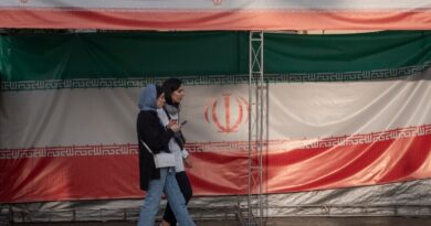 Two young Iranian women walk past the country's flags in northern Tehran, Iran, on June 30, 2025, following the ceasefire between Iran and Israel.