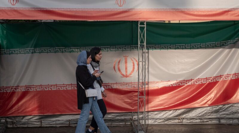 Two young Iranian women walk past the country's flags in northern Tehran, Iran, on June 30, 2025, following the ceasefire between Iran and Israel.