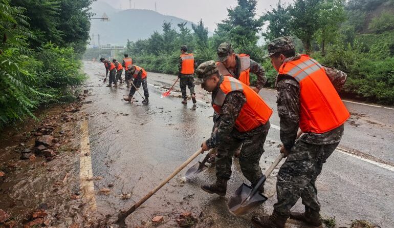 In this photo released by Xinhua News Agency, members of the Chinese People's Armed Police Force clean up silt on a road in Miyun District as continuous rain fall triggers alerts, in north of Beijing on July 27, 2025. (Wang Xiqing/Xinhua via AP)