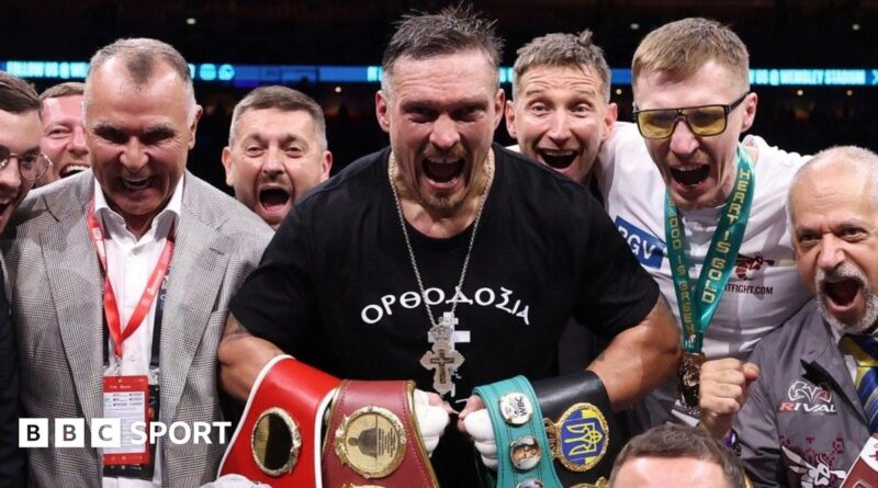 Oleksandr Usyk holds up his arms as Daniel Dubois walks past in the ring at Wembley Stadium