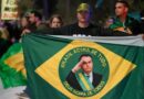 Protesters hold up a Brazilian flag with Bolsonaro's face in the middle.