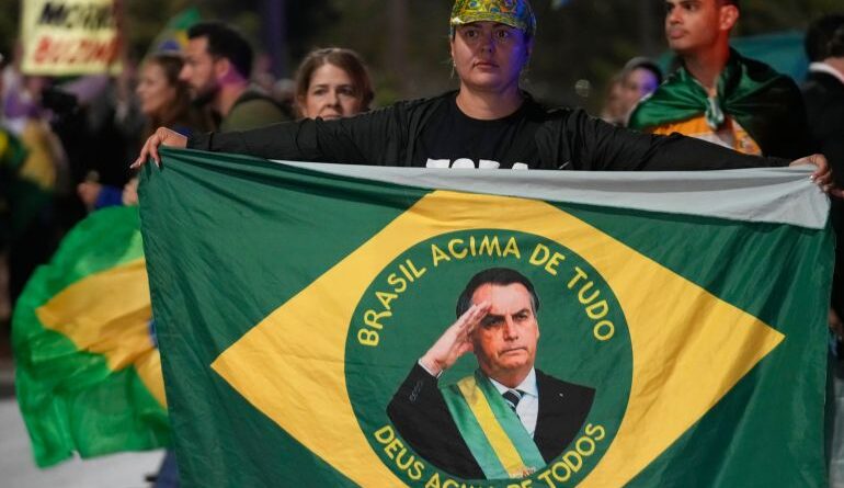 Protesters hold up a Brazilian flag with Bolsonaro's face in the middle.