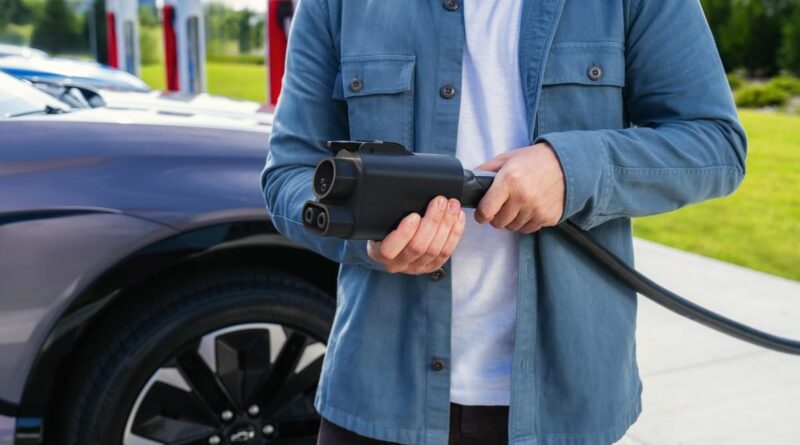 A man holds a Tesla charging cable with a CCS adapter attached.