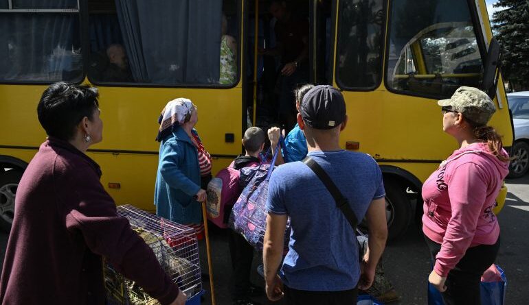 people carrying their belongings get onto a yellow bus