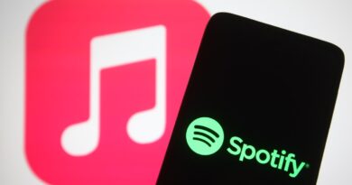 The Spotify logo seen displayed on a smartphone screen in front of Apple Music logo in the background.