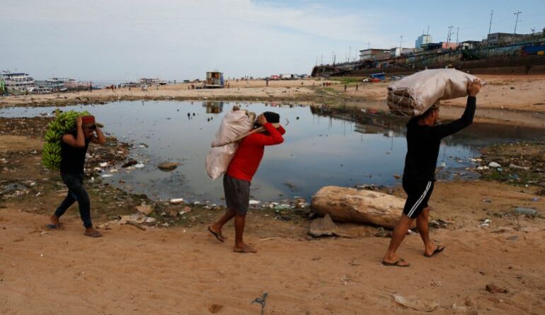 FILE - Porters carry goods brought by boat across a dry area of the Negro River at the port in Manaus, Amazonas state, Brazil, Oct. 4, 2024, amid a severe drought. (AP Photo/Edmar Barros, File)