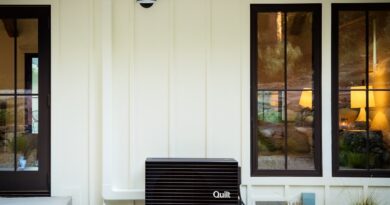 A Quilt heat pump outdoor unit sits outside a white house.