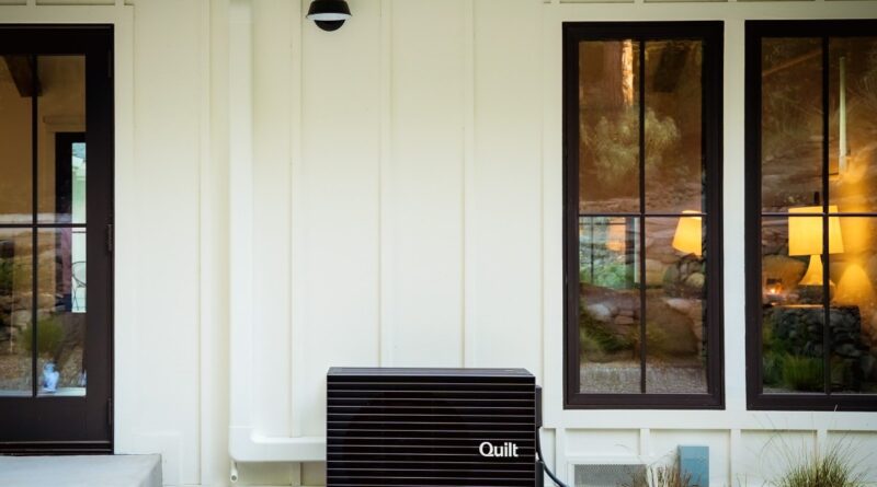 A Quilt heat pump outdoor unit sits outside a white house.
