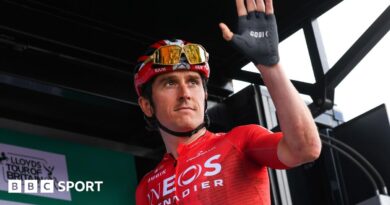 Geraint Thomas wears a red top and black shorts and he cycles past crowds of people
