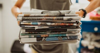 A person holding a pile of newspapers.