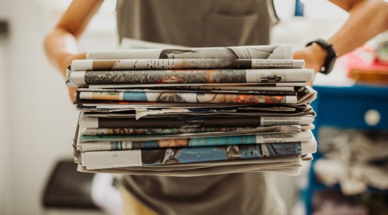A person holding a pile of newspapers.