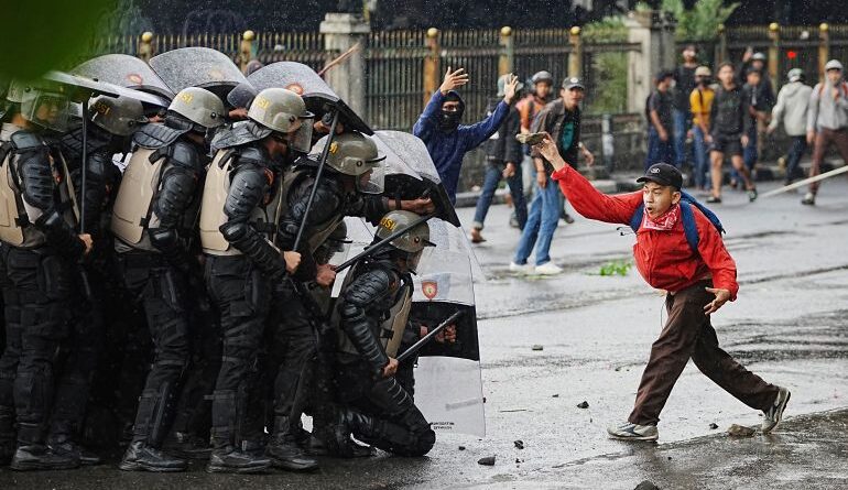 A protester throws rock at riot police officers during a protest against lavish allowances given to parliament members, in Jakarta, Indonesia, Thursday, Aug. 28, 2025. (AP Photo/Achmad Ibrahim)