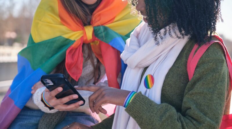 Two young women are using a smartphone while showing their support for LGBTQ+ rights