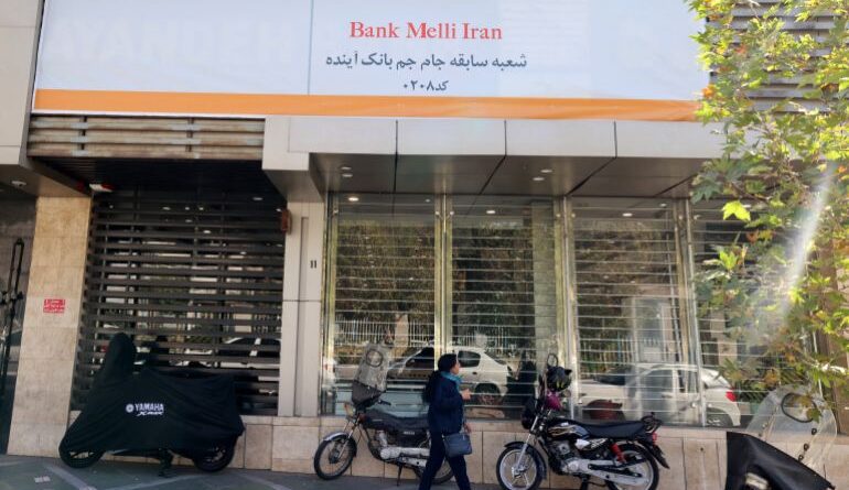 An Iranian woman walks past a branch of the state-owned Melli Bank, which absorbed the assets of the now-defunct Ayandeh Bank, with signage on its facade reading in Farsi "This former Ayandeh Bank branch is now part of Melli Bank"in the capital Tehran on October 25, 2025.