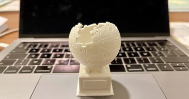 A 3D-printed version of the Wikipedia logo rests on the touchpad of an open MacBook.