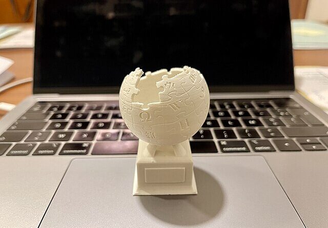 A 3D-printed version of the Wikipedia logo rests on the touchpad of an open MacBook.