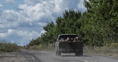 Ukrainian soldiers ride a military vehicle with Russian POWs in the truck bed.
