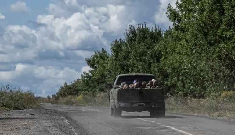 Ukrainian soldiers ride a military vehicle with Russian POWs in the truck bed.