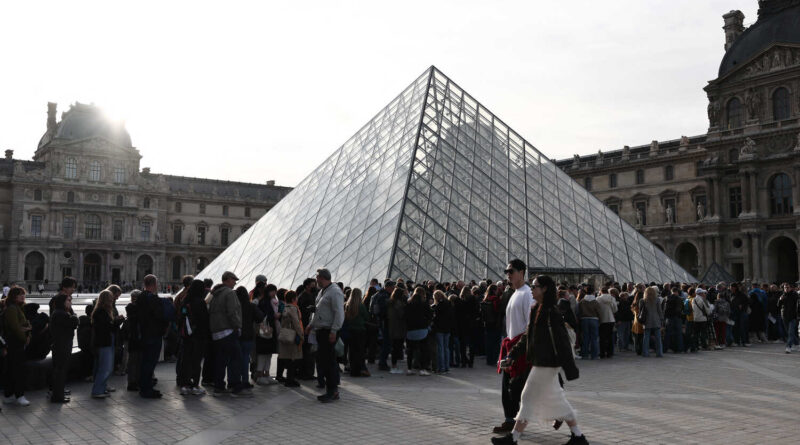 Lines of people outside the glass pyramid at the Louvre Museum in Paris.