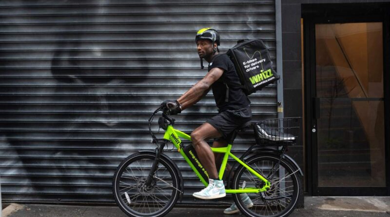 Side shot of food delivery worker on Whizz e-bike on NYC street in front of street mural