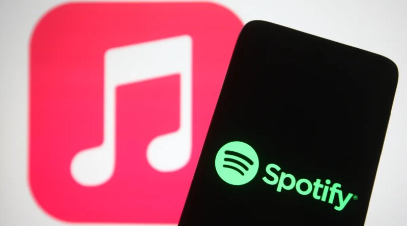 The Spotify logo seen displayed on a smartphone screen in front of Apple Music logo in the background.