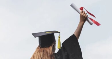 Rear view of woman in a cap and gown holding a diploma in the air.