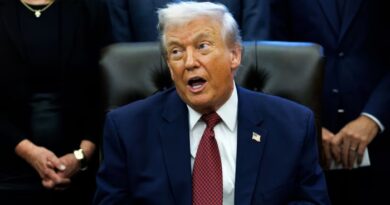 Donald Trump speaks while seated at a desk, surrounded by people, during the announcement of changes to fuel economy standards.