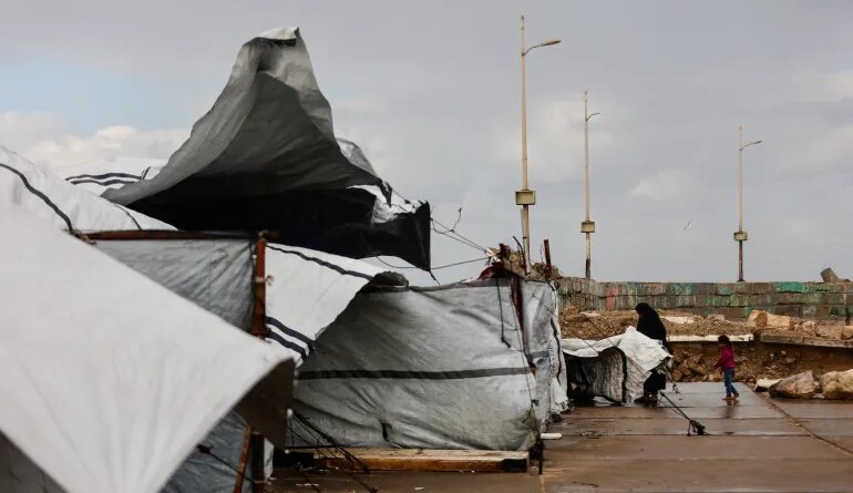 A displaced Palestinian woman adjusts the canvas of the family tent shelter as the region experiences rain and cold winter conditions, in Gaza City on December 28, 2025.