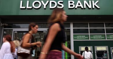Pedestrians pass by a Lloyds Bank branch in London as a person uses an ATM outside the building.