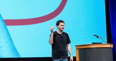 Jonathan Ross stands on stage speaking and gesturing with one hand raised at the GenAI Summit, with a microphone and podium nearby.
