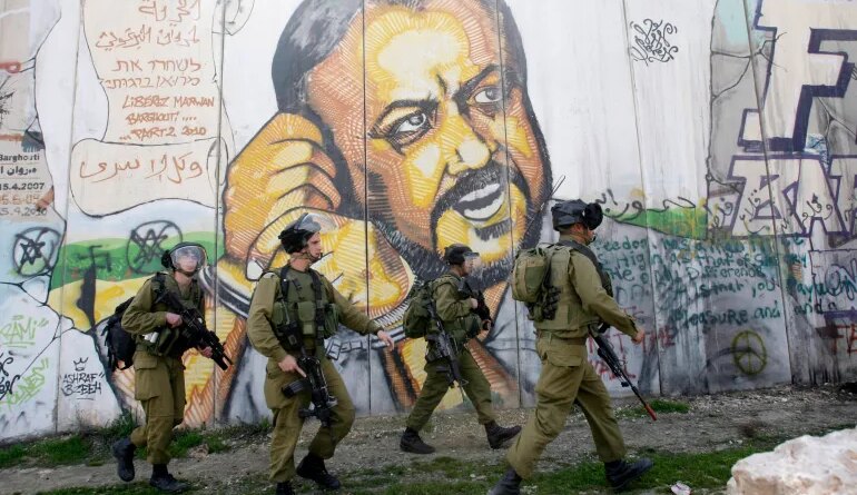 In the background of part of Israel's separation barrier with portrait of jailed Fatah leader Marwan Barghouti, Israeli soldiers patrol at Kalandia checkpoint between Jerusalem and the West Bank city of Ramallah,