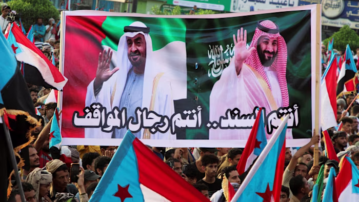 People at a rally hold a large banner with images of Sheikh Mohamed bin Zayed al-Nahyan and Mohammed bin Salman.
